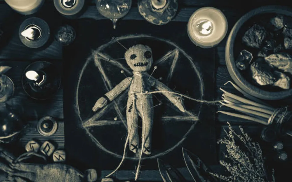 Voodoo doll placed on a pentagram chalk design, surrounded by candles, pins, and ritualistic tools
