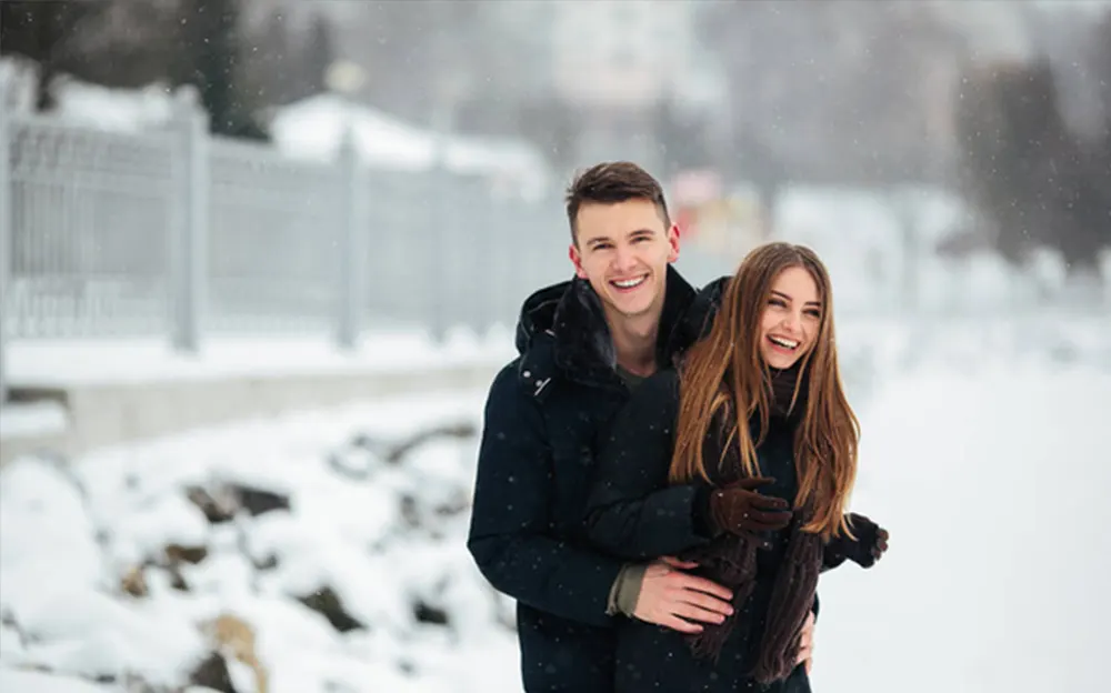 Smiling couple enjoying a snowy day outdoors, embracing each other warmly