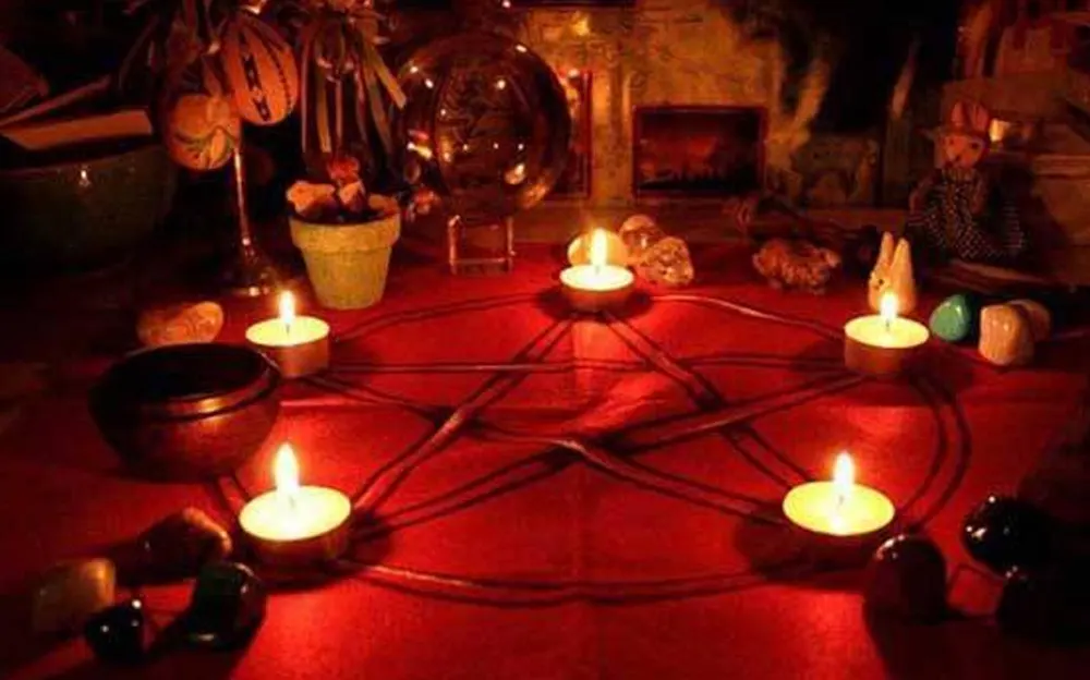 A ritual setup featuring a glowing pentagram with candles, crystals, and mystical objects on a red surface, evoking a spiritual or mystical atmosphere